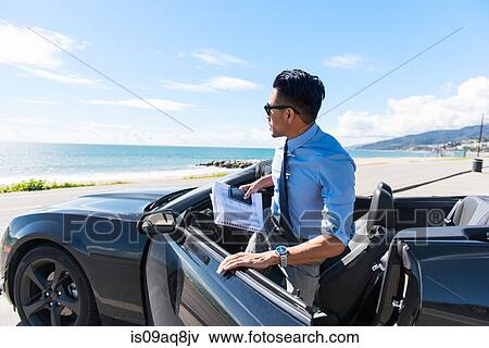 Young businessman getting out of car at coastal parking lot with paperwork View Large Photo Image Stock Photo - Young businessman getting out of car at coastal parking lot with paperwork. Fotosearch