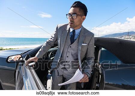 Young businessman getting out of car at coastal parking lot with paperwork and smartphone View Large Photo Image Stock Photo - Young businessman getting out of car at coastal parking lot with paperwork and smartphone. Fotosearch