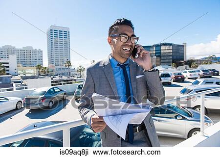 Young businessman on city rooftop car park smiling whilst talking on smartphone View Large Photo Image Stock Image - Young businessman on city rooftop car park smiling whilst talking on smartphone. Fotosearch