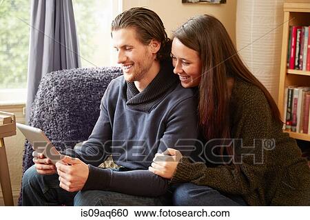 Young couple browsing digital tablet in living room View Large Photo Image Stock Image - Young couple browsing digital tablet in living room. Fotosearch