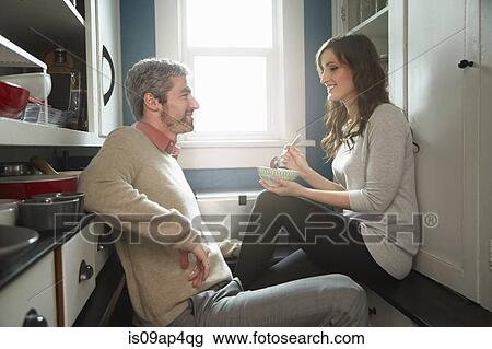 Stock Image - Young couple having breakfast opposite each other in kitchen. Fotosearch