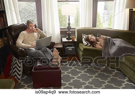 Young couple in sitting room using smartphone and laptop View Large Photo Image Stock Photo - Young couple in sitting room using smartphone and laptop. Fotosearch