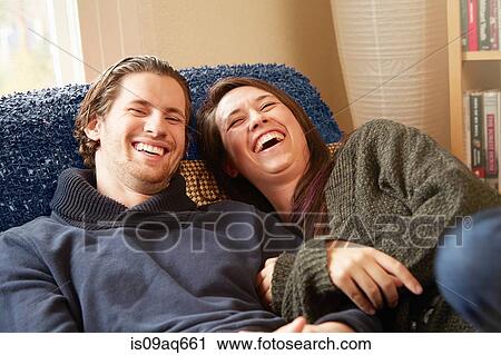 Young couple laughing on living room sofa View Large Photo Image Stock Image - Young couple laughing on living room sofa. Fotosearch