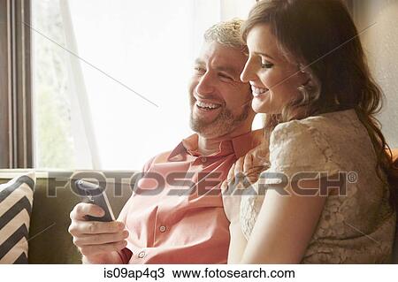 Stock Image - Young couple on sitting room sofa reading smartphone texts. Fotosearch