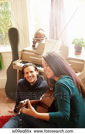 Young couple playing acoustic guitar in living room View Large Photo Image Stock Photo - Young couple playing acoustic guitar in living room. Fotosearch