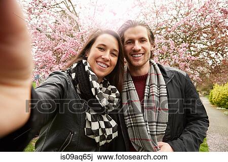 Young couple posing for selfie with blossom in park View Large Photo Image Stock Image - Young couple posing for selfie with blossom in park. Fotosearch