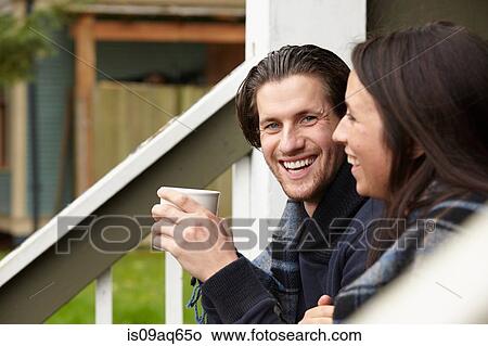 Picture - Young couple sitting on porch step drinking coffee. Fotosearch
