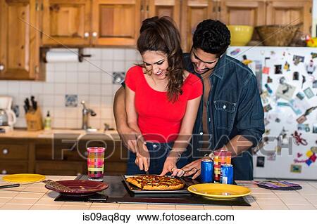 Stock Photo - Young couple slicing pizza in kitchen. Fotosearch