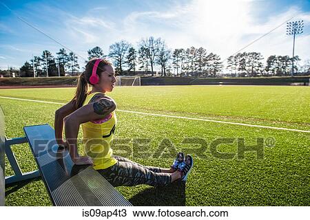 Stock Image - Young female athlete doing reverse push ups on sports field bench. Fotosearch