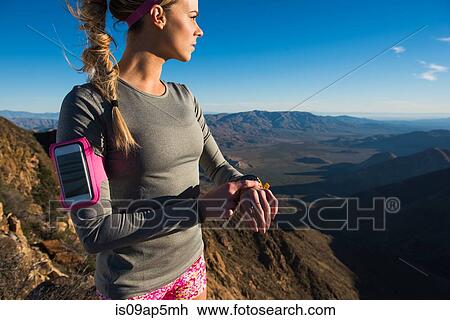 Stock Image - "Young female trail runner checking stopwatch on Pacific Crest Trail, Pine Valley, California, USA". Fotosearch