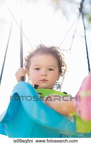 Stock Image - "Young girl on playground swing, low angle view". Fotosearch