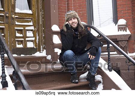 Young man chatting on smartphone on snow covered front door step View Large Photo Image Stock Photography - Young man chatting on smartphone on snow covered front door step. Fotosearch
