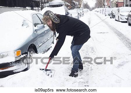 Stock Photograph - Young man clearing snow from road with shovel. Fotosearch