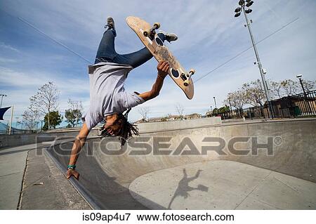 Stock Photo - Young man doing skateboard trick upside down on edge of skateboard park. Fotosearch