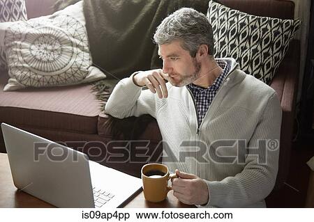 Stock Photography - Young man drinking coffee and browsing laptop. Fotosearch
