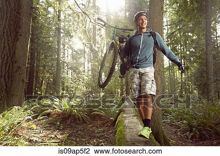 Stock Image - "Young man in forest, carrying mountain bike over fallen tree". Fotosearch
