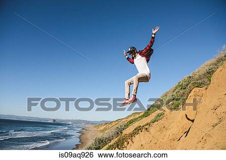 "Young man jumping down sandy hill, in mid air" View Large Photo Image Stock Photograph - "Young man jumping down sandy hill, in mid air". Fotosearch