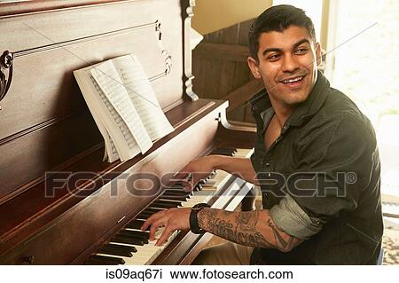 Stock Image - Young man looking over his shoulder whilst playing piano. Fotosearch