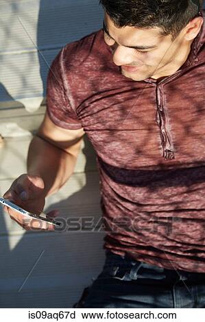 Young man reading smartphone text on park bench View Large Photo Image Stock Image - Young man reading smartphone text on park bench. Fotosearch