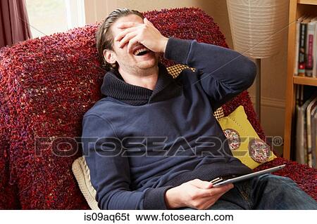 Young man reclining on sofa covering his face whilst laughing View Large Photo Image Stock Photograph - Young man reclining on sofa covering his face whilst laughing. Fotosearch
