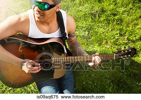 Young man sitting on grass playing acoustic guitar View Large Photo Image Stock Photography - Young man sitting on grass playing acoustic guitar. Fotosearch