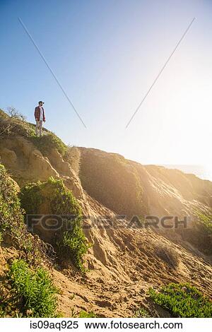 "Young man standing at top of sandy hill, looking at view" View Large Photo Image Stock Photography - "Young man standing at top of sandy hill, looking at view". Fotosearch