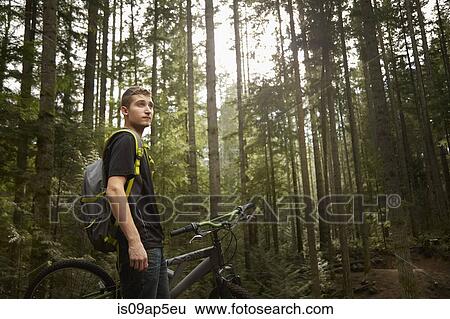 "Young man standing beside mountain bike, in forest" View Large Photo Image Stock Photograph - "Young man standing beside mountain bike, in forest". Fotosearch