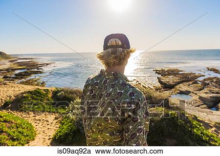 "Young man standing, looking at ocean, rear view" View Large Photo Image Stock Image - "Young man standing, looking at ocean, rear view". Fotosearch