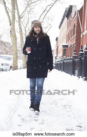 Young man strolling along snow covered street drinking takeaway coffee View Large Photo Image Picture - Young man strolling along snow covered street drinking takeaway coffee. Fotosearch