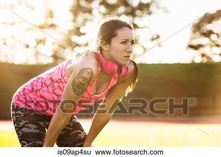 Stock Photograph - Young tattooed female athlete taking a break on sports field. Fotosearch