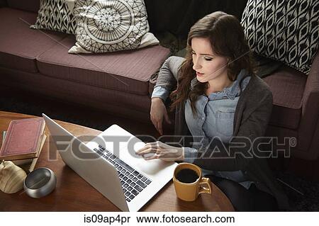 Stock Photography - Young woman drinking coffee and browsing laptop. Fotosearch