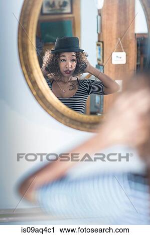Young woman looking in wall mirror trying on fedora View Large Photo Image Stock Image - Young woman looking in wall mirror trying on fedora. Fotosearch