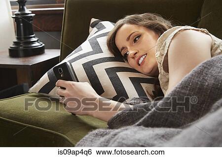 Young woman lying on living room sofa reading smartphone texts View Large Photo Image Stock Photograph - Young woman lying on living room sofa reading smartphone texts. Fotosearch