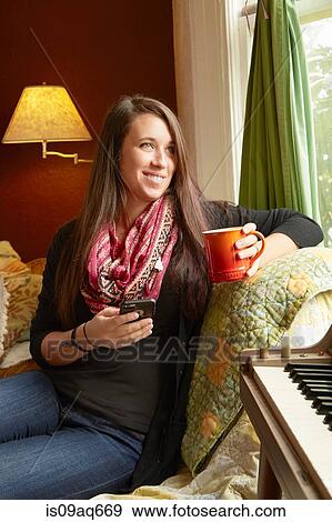 Young woman reclining on sofa looking out of window whilst drinking coffee View Large Photo Image Stock Photo - Young woman reclining on sofa looking out of window whilst drinking coffee. Fotosearch