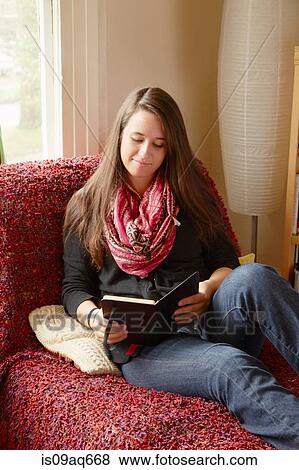 Stock Photo - Young woman reclining on sofa reading a book. Fotosearch