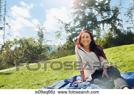 Stock Photo - Young woman sitting on picnic blanket in park. Fotosearch