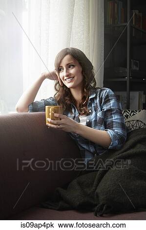 Young woman sitting on sofa drinking coffee View Large Photo Image Stock Image - Young woman sitting on sofa drinking coffee. Fotosearch