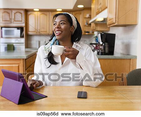 Young woman using digital tablet at kitchen table View Large Photo Image Stock Image - Young woman using digital tablet at kitchen table. Fotosearch