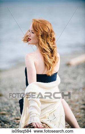 Picture - "Young woman with long red hair looking over her shoulder on beach, Bainbridge Island, Washington State, USA". Fotosearch