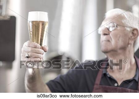 Brewer in brewery holding up a glass of beer View Large Photo Image Picture - Brewer in brewery holding up a glass of beer. Fotosearch