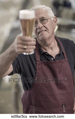 Brewer in brewery holding up a glass of beer View Large Photo Image Stock Photograph - Brewer in brewery holding up a glass of beer. Fotosearch