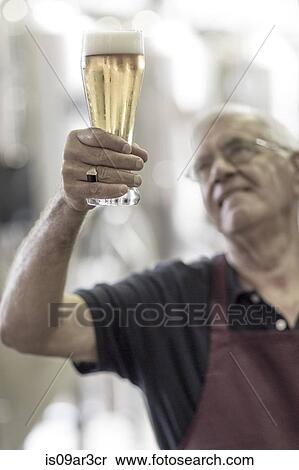Brewer in brewery holding up a glass of beer View Large Photo Image Stock Photography - Brewer in brewery holding up a glass of beer. Fotosearch
