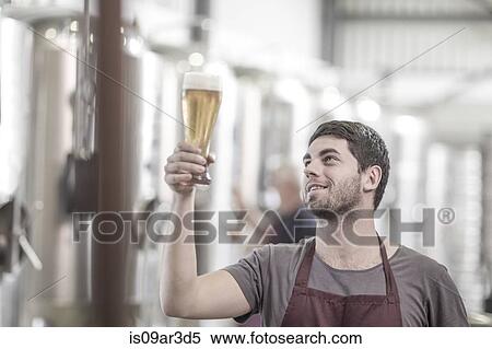Brewer in brewery holding up a glass of beer View Large Photo Image Stock Photography - Brewer in brewery holding up a glass of beer. Fotosearch