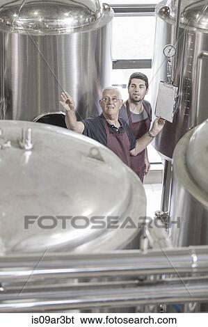 Stock Photograph - Brewers in brewery next to stainless steel tanks. Fotosearch
