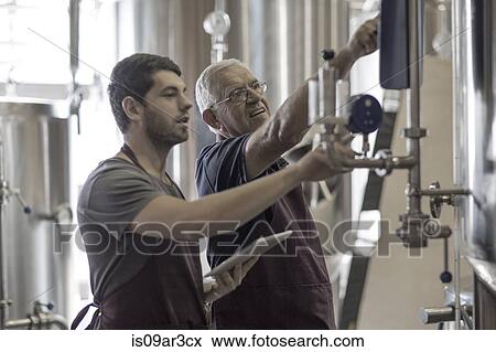 Stock Photo - Brewers in brewery standing next to stainless steel tanks. Fotosearch
