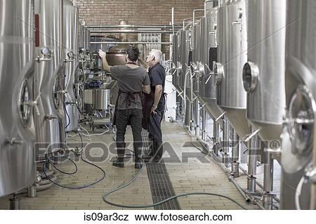Brewers in brewery standing next to stainless steel tanks View Large Photo Image Stock Photo - Brewers in brewery standing next to stainless steel tanks. Fotosearch