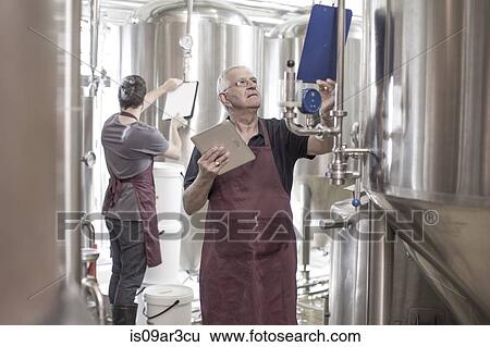 Stock Photograph - Brewers in brewery standing next to stainless steel tanks. Fotosearch