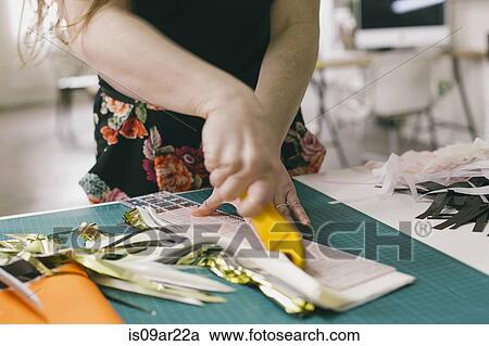 Stock Image - Close up of female textile designer cutting textiles in design studio. Fotosearch