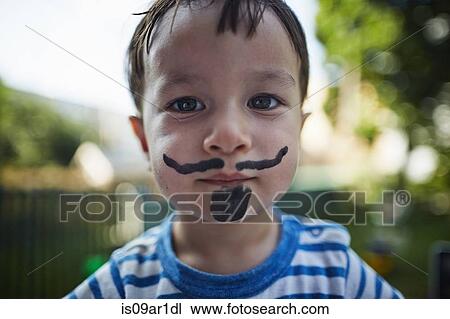 Stock Image - Close up portrait of boy looking at camera wearing beard and moustache face paint costume. Fotosearch