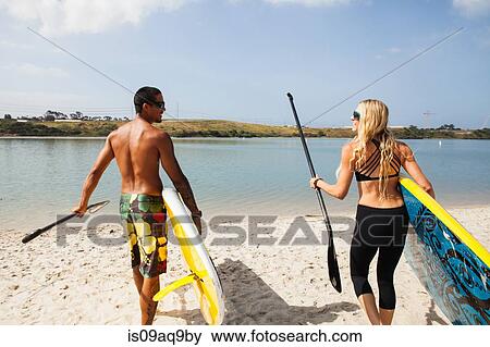 "Couple carrying paddleboards on beach, Carlsbad, California, USA" View Large Photo Image Stock Photo - "Couple carrying paddleboards on beach, Carlsbad, California, USA". Fotosearch